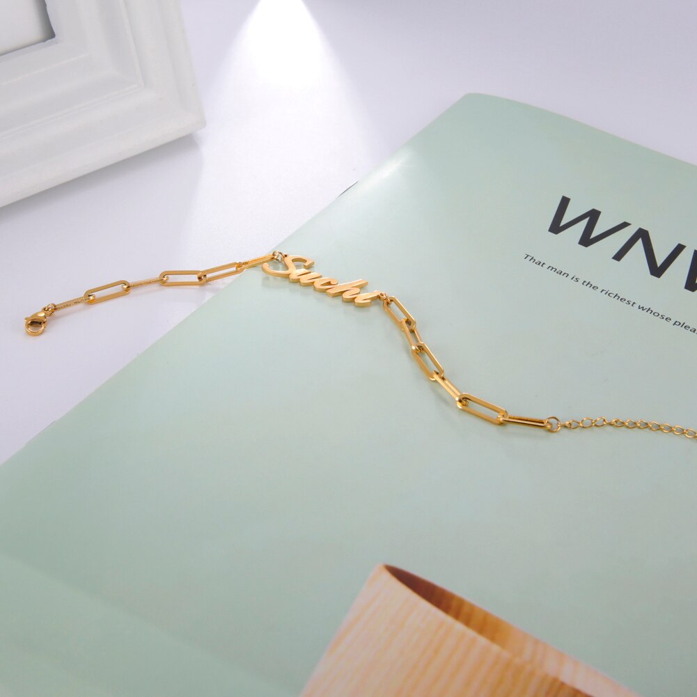 Chain links name bracelet in gold metal alloy on magazine page.