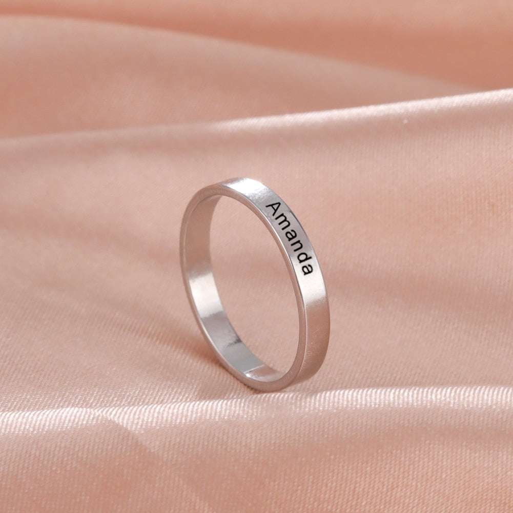 Custom engraved silver ring with personalized name on satin fabric.