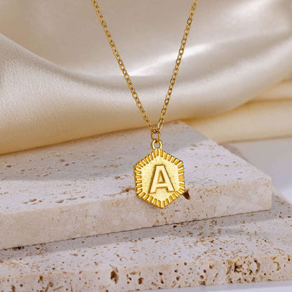 YourLetter Hexagon Embossed Necklace with gold finish on marble surface.