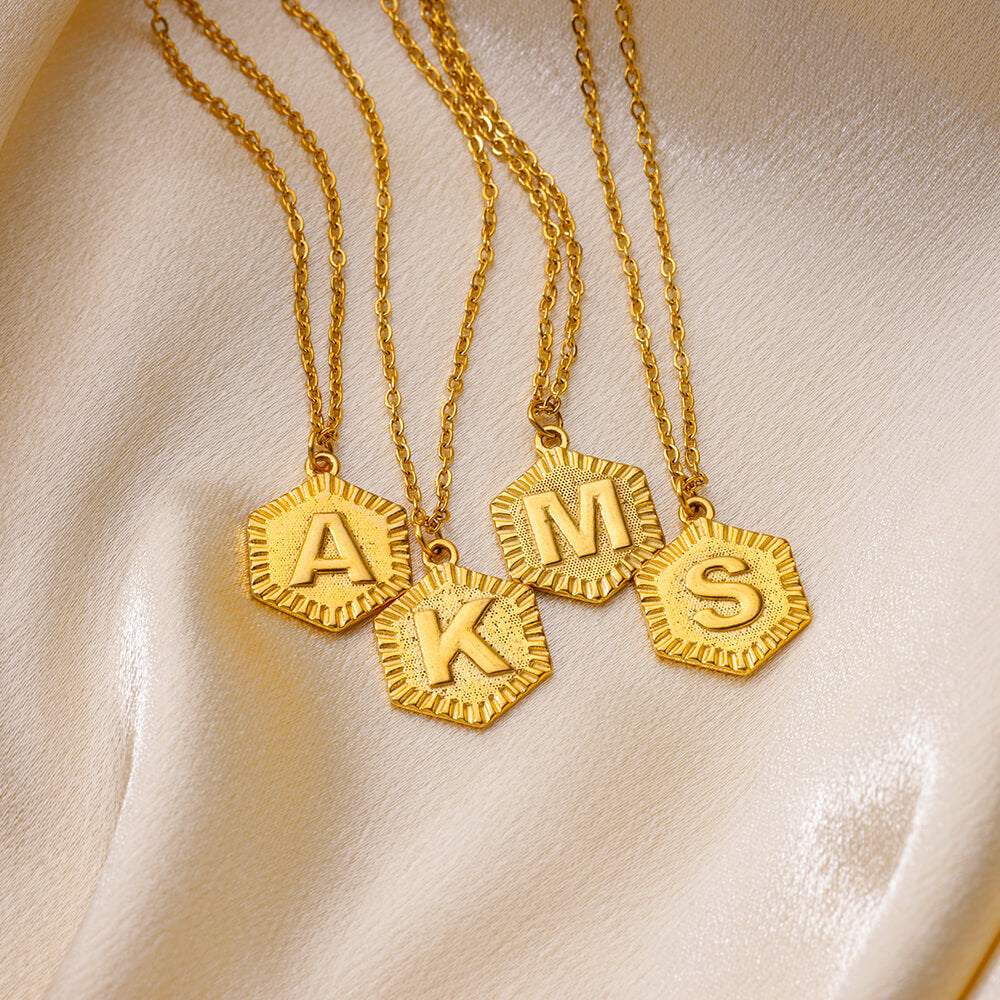 YourLetter Hexagon Embossed Necklace with gold finish and embossed letters on satin background.